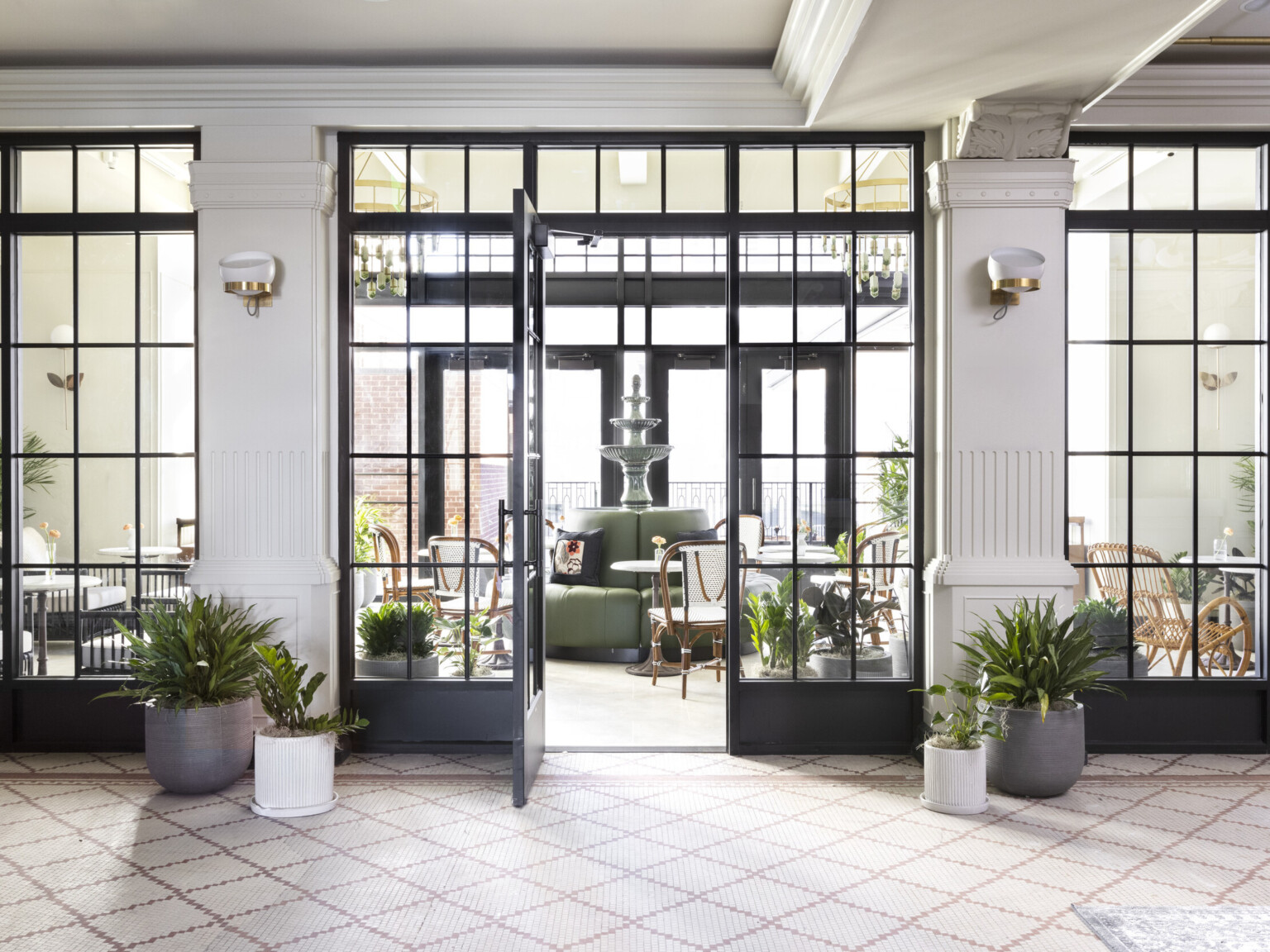 Floor to ceiling windows with door opened to seating area with fountain in round sofa. Room framed by white columns and plants