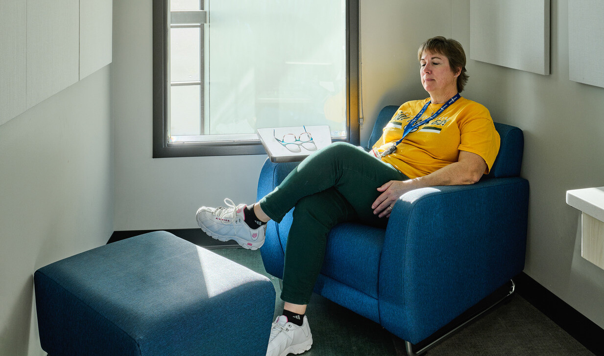 Small seating area with a person in a yellow shirt relaxing in a blue chair in front of a large window