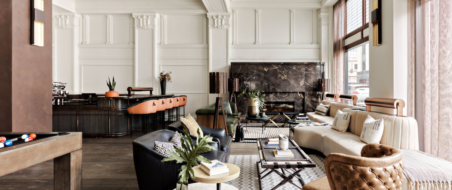 Seating area with arm chairs and cushioned bench along windows. Dark marbled fireplace on white wall with pillars and molding