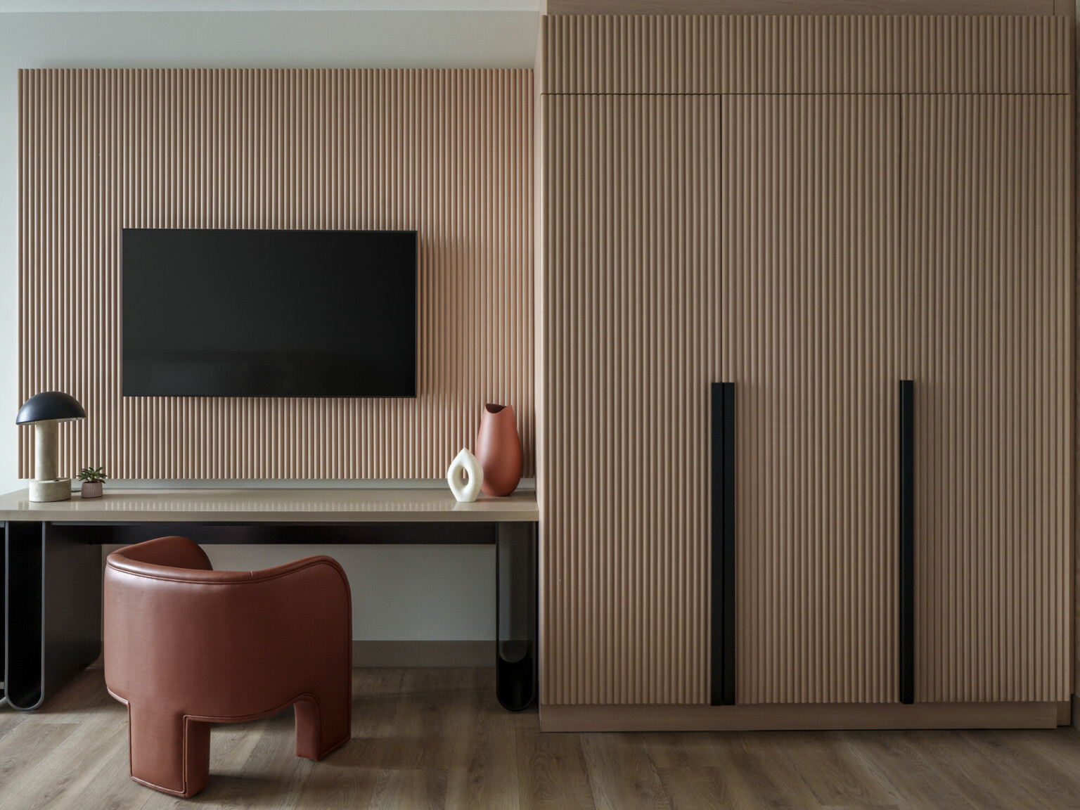 Modern hotel room desk area showing a wooden accent back drop, desk with chair and TV hanging on wall and cabinets to the right