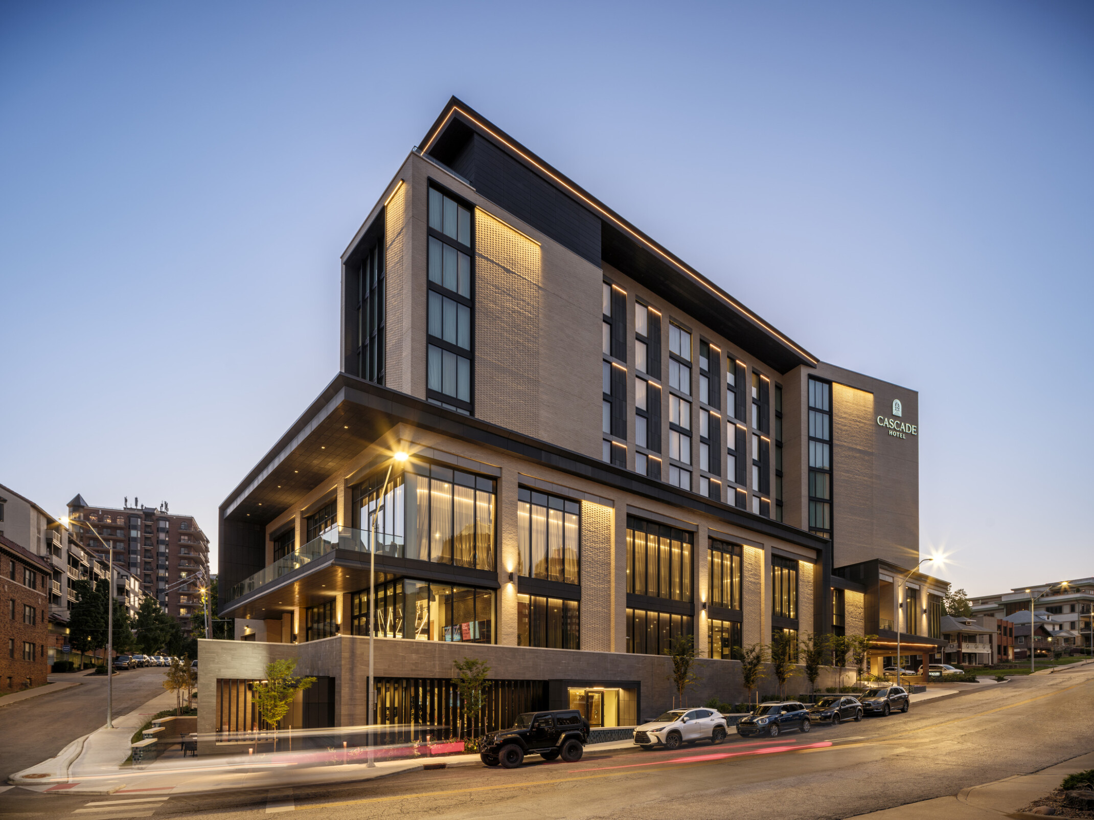 Exterior of a modern neutral brick multistory hotel at dusk filled with dimly lit windows and sign in top right corner that says Cascade Hotel