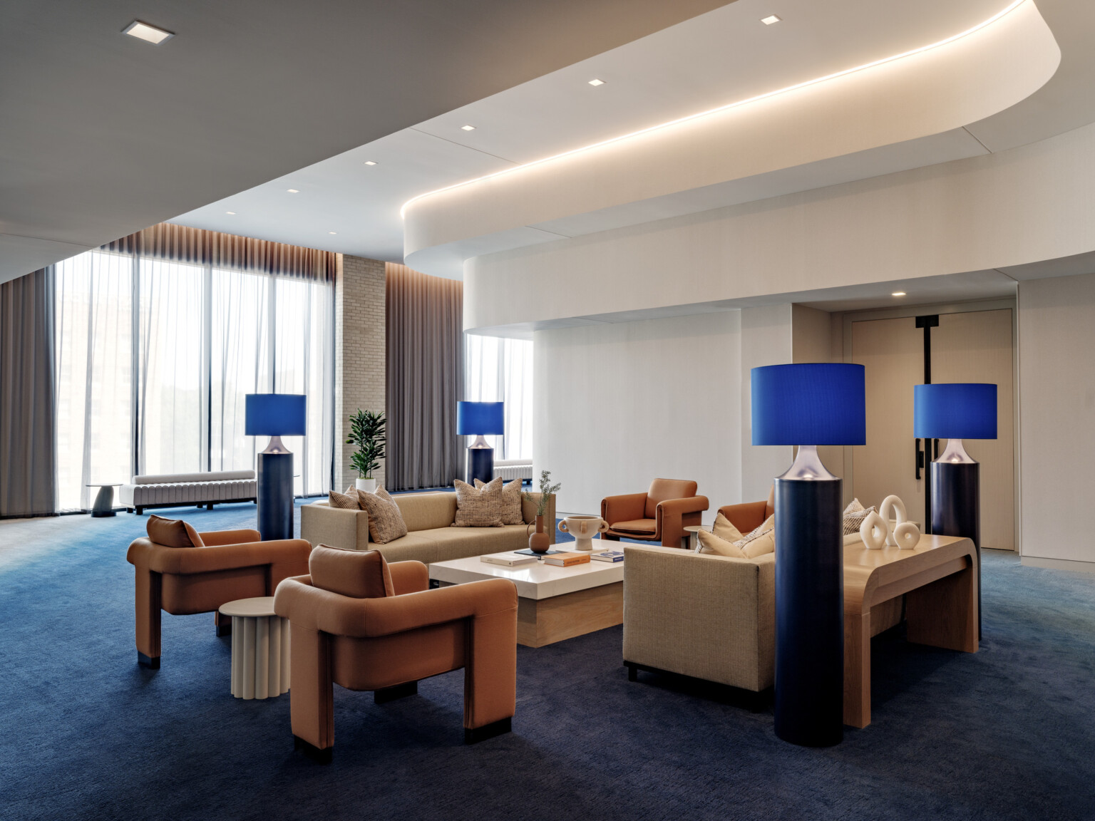 hotel public seating area with midcentury modern furniture in orange; blue carpet and blue floor lamps bring a pop of color; curved custom ceiling detail and lighting elevate space