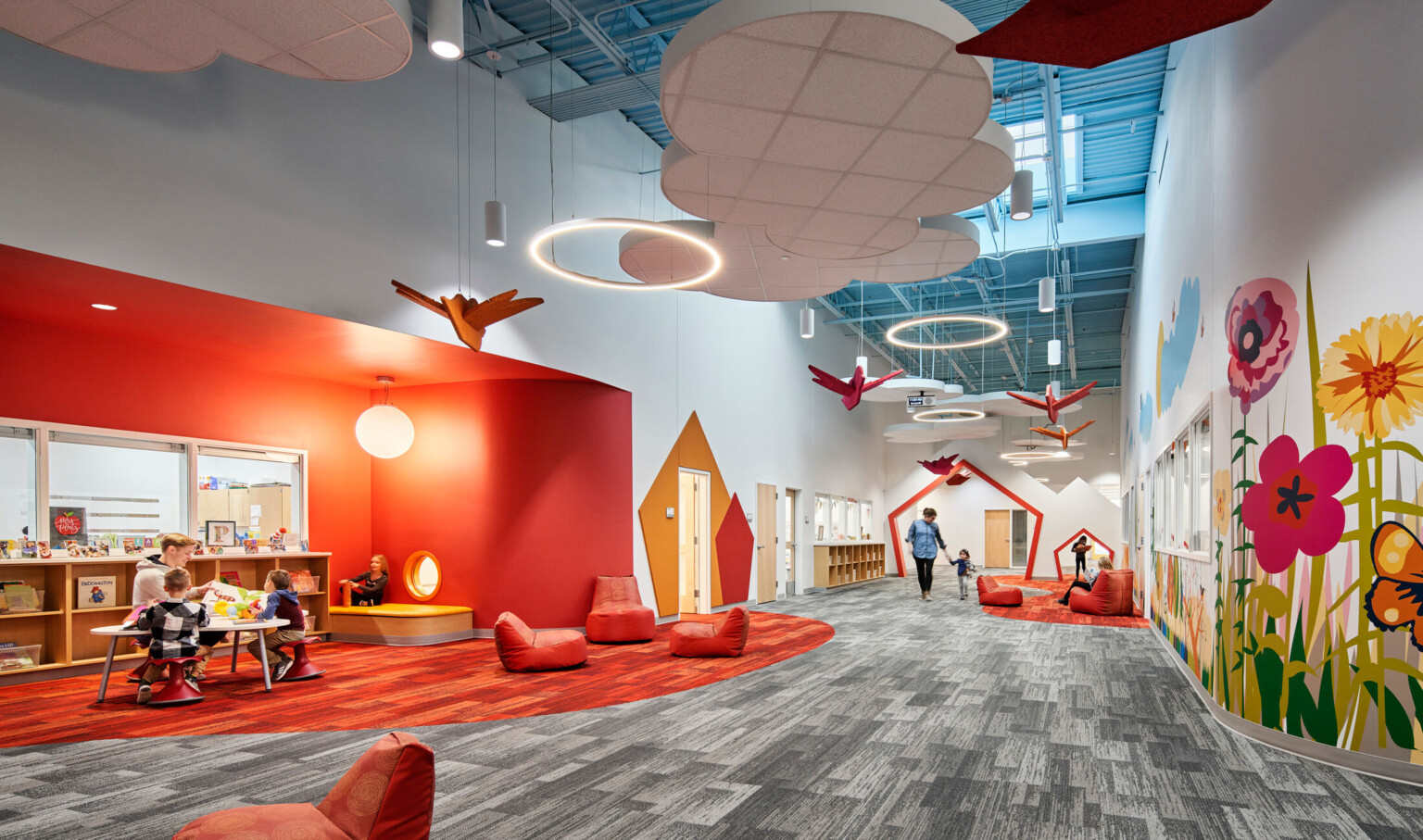 high blue ceilings and grey geometric print carpet with suspended cloud and orange bird elements, bright orange accent wall, mural with brightly colored flowers