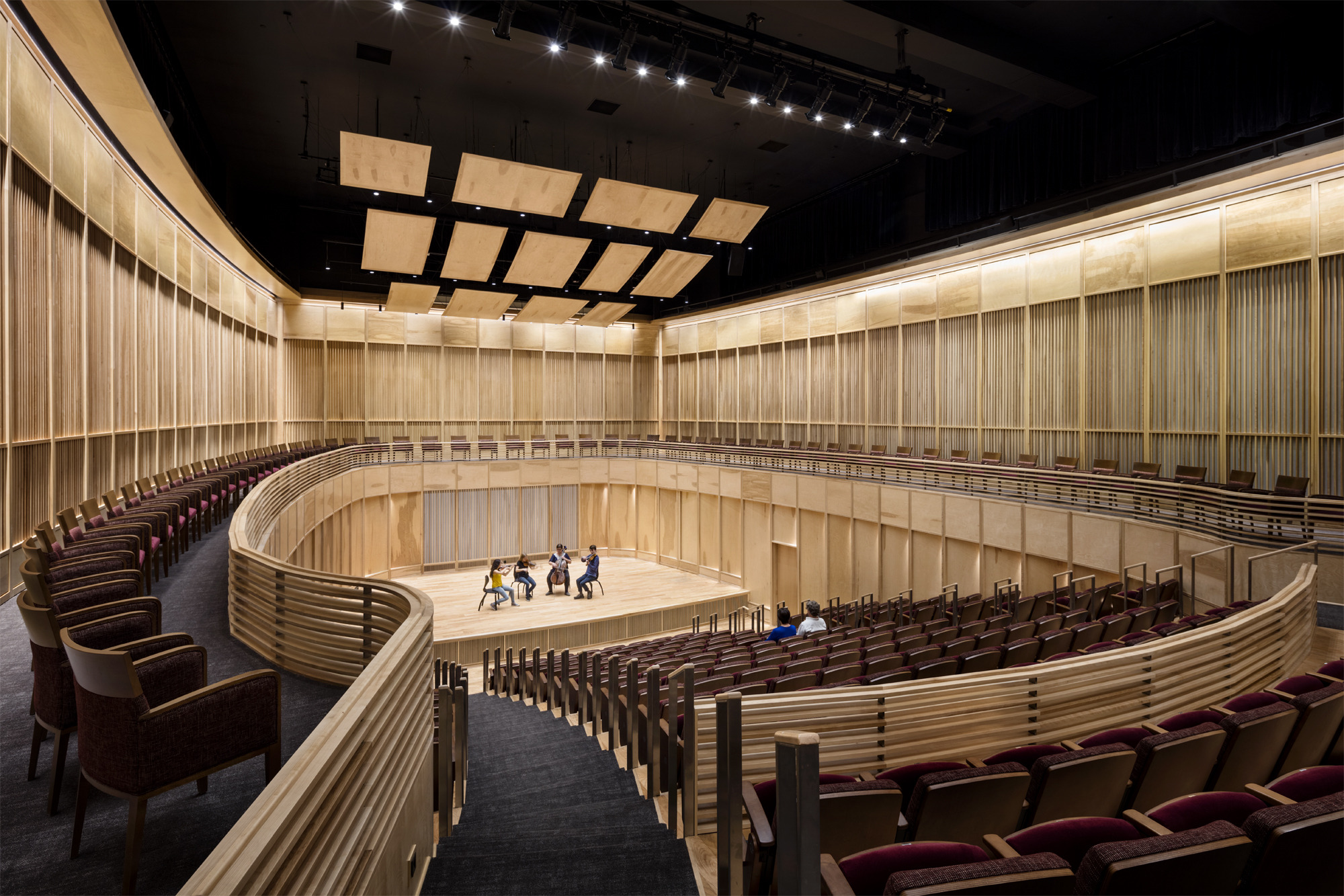 View from the back of wooden wall oval auditorium with 4 musicians on stage and 2 people seated in the audience