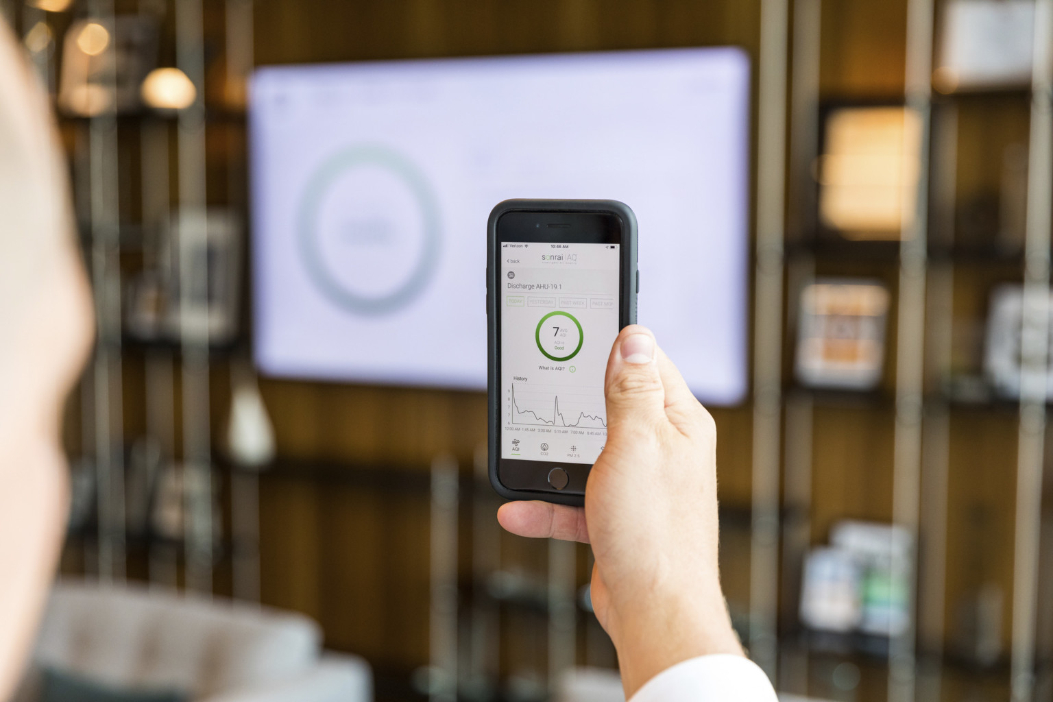 person using sonrai IAQ app in a space to read live air quality metrics, which are also shown on the lobby screen in front