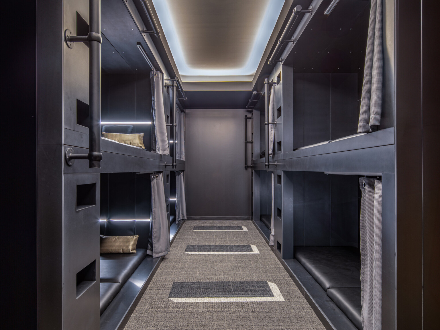 Hallway lined with sleeping pods on top and bottom made of dark wood on each side with curtains and handrails