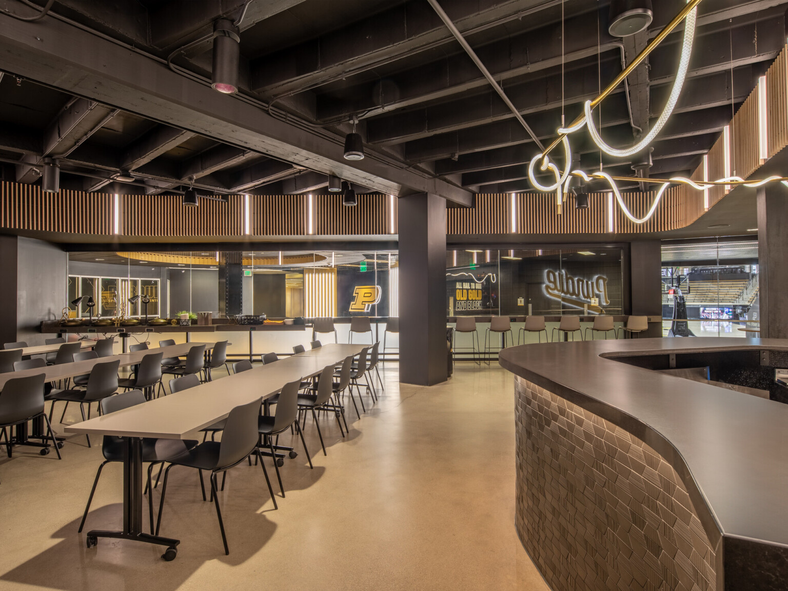 Lunchroom with black ceiling and walls filled with rectangular tables and chairs with Purdue logo on back wall and large counter area