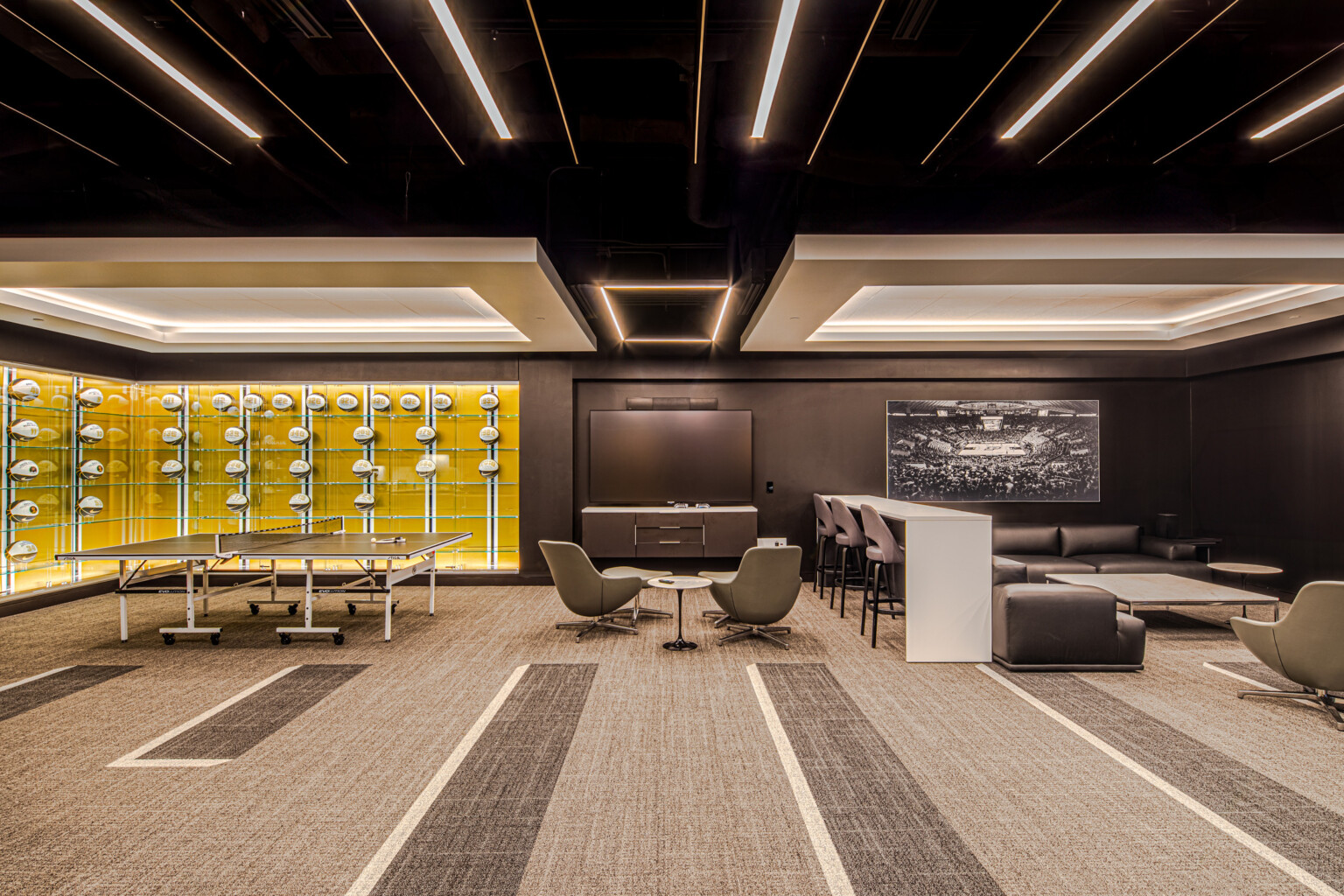 Lounge area featuring glass cases filled will basketballs with a yellow wall, multiple seating areas divided by a bar height table and chairs