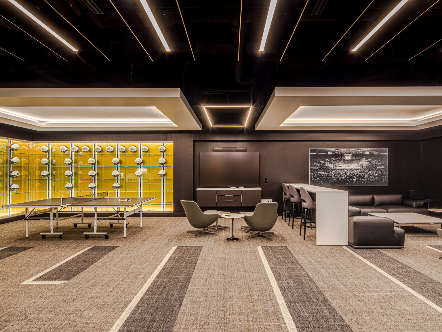 Lounge area featuring glass cases filled will basketballs with a yellow wall, multiple seating areas divided by a bar height table and chairs