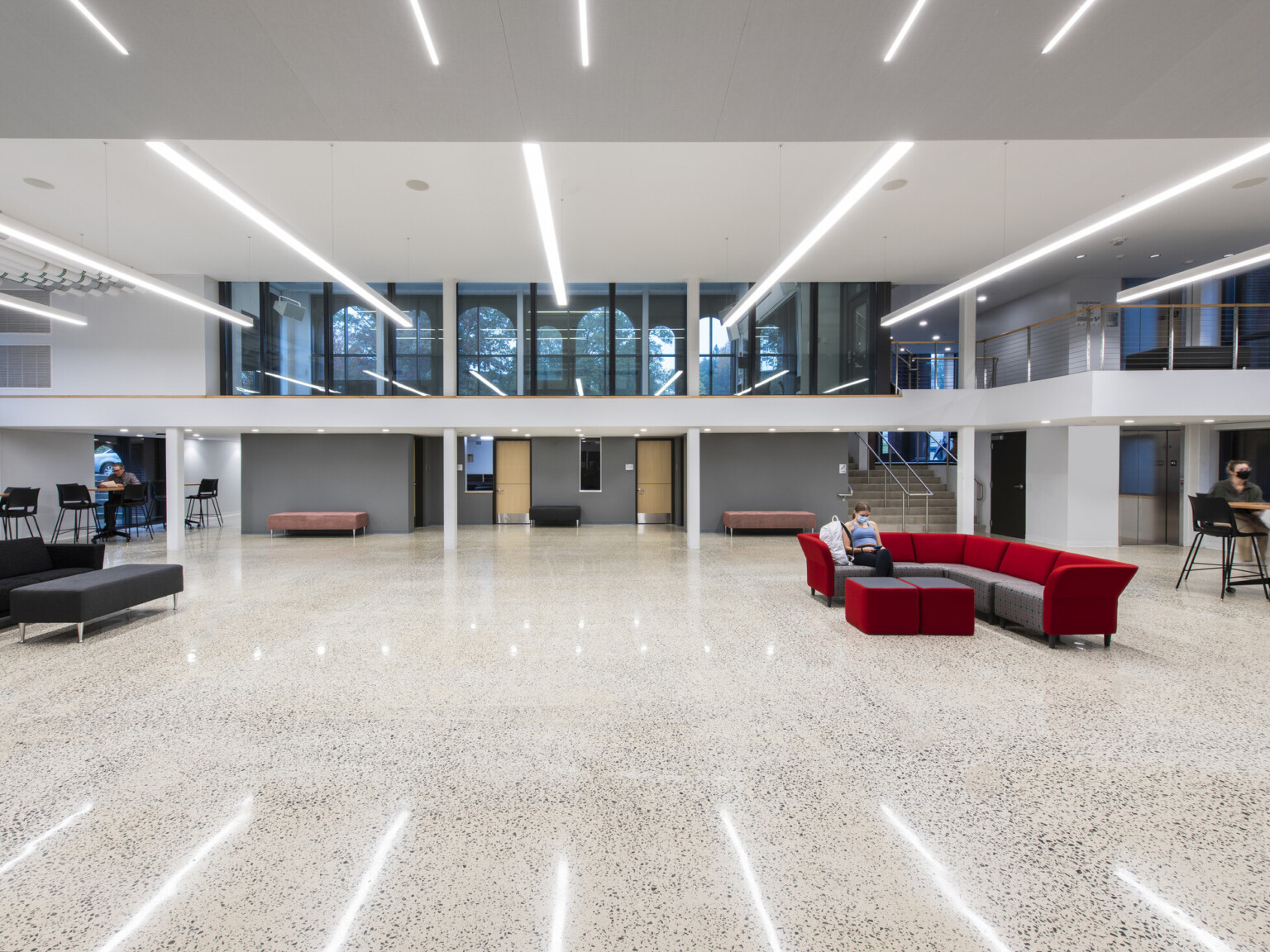 Large multistory common area with multiple seating areas around the perimeter, red couch in the middle, large windows on the second story overlooking the first floor.