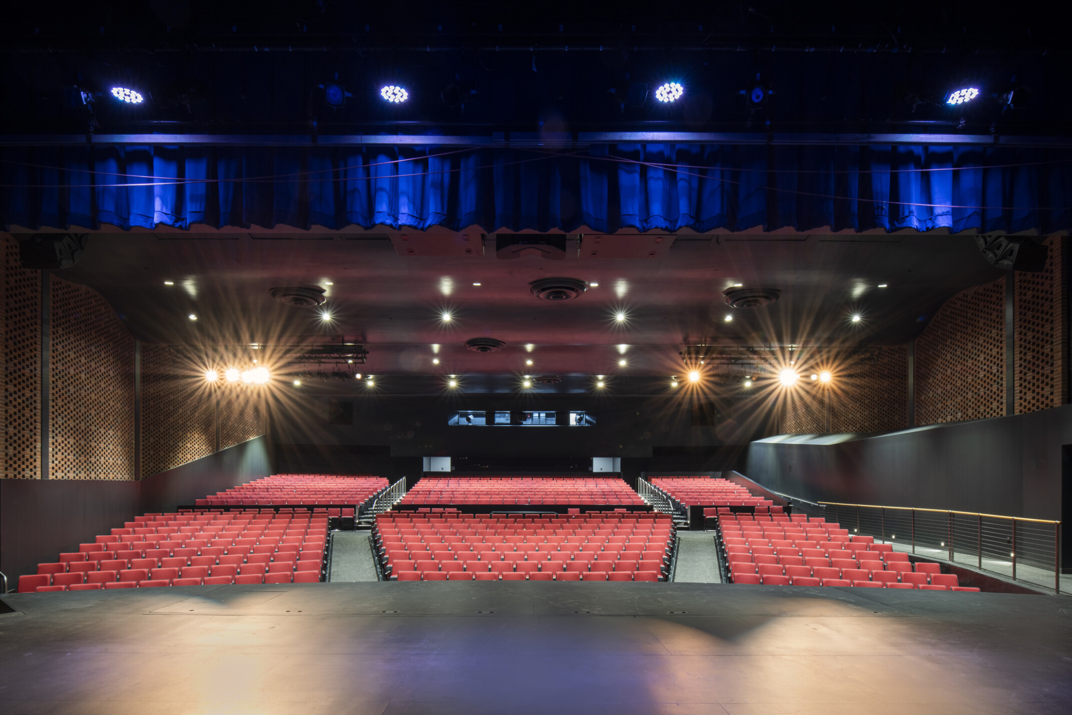 Theatre auditorium showing rows of red seats, black walls with wooden accents, and bright lights making starburst shapes.