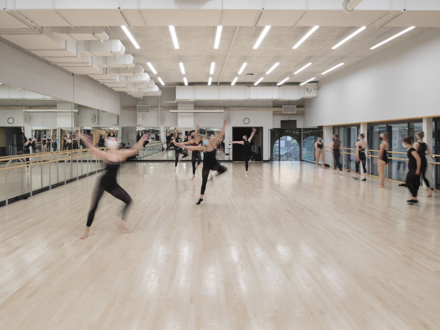 Dance room showing light wood floors, a wall of mirrors, filled with dancers dressed in black