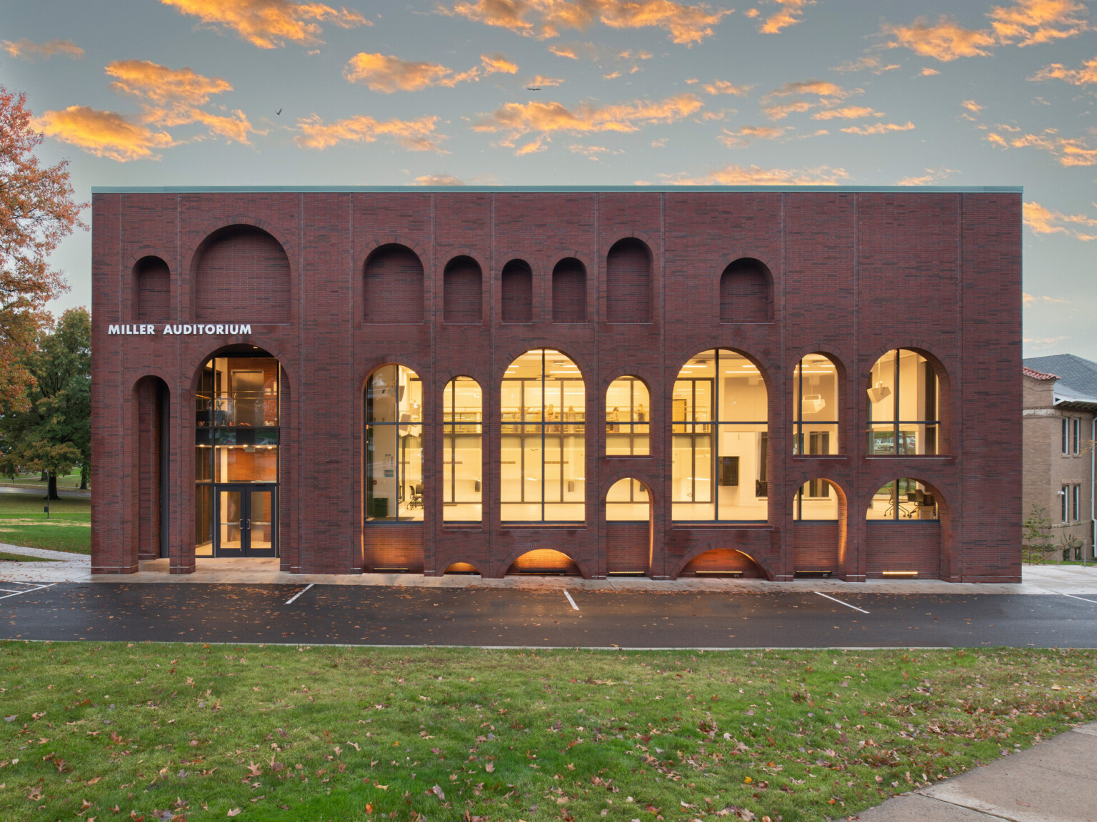 Brick multistory building with arched windows filled with light and words Miller Auditorium in white letters on the left above the doorway