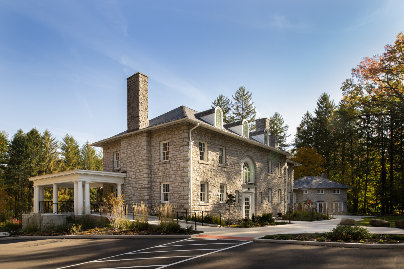 Stone façade mansion nestled in lush, tall trees, greenery, blue skies