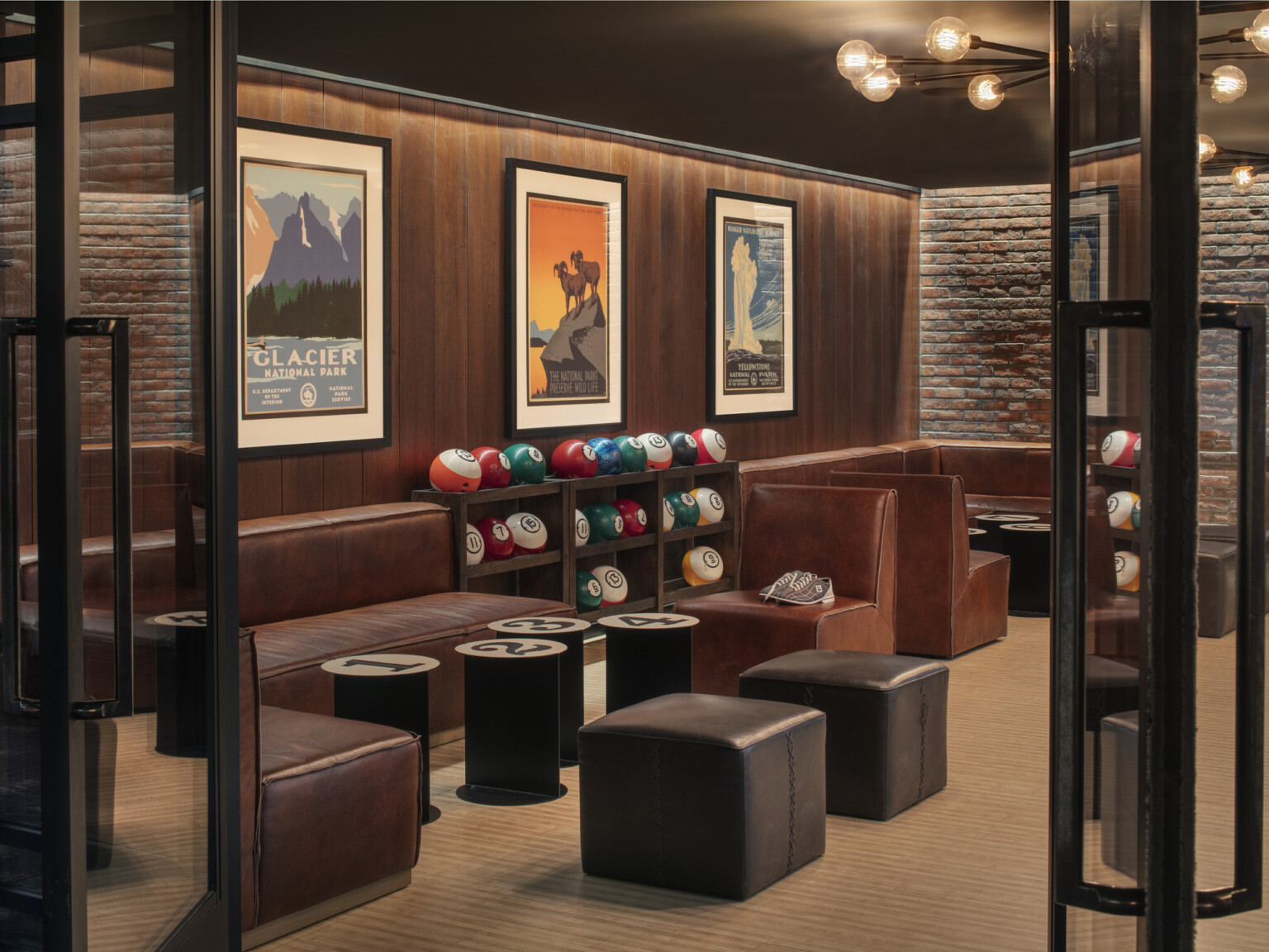 A cozy room with leather booths along the wood lined walls, vintage posters, numbered tables, and racks of bowling balls on display