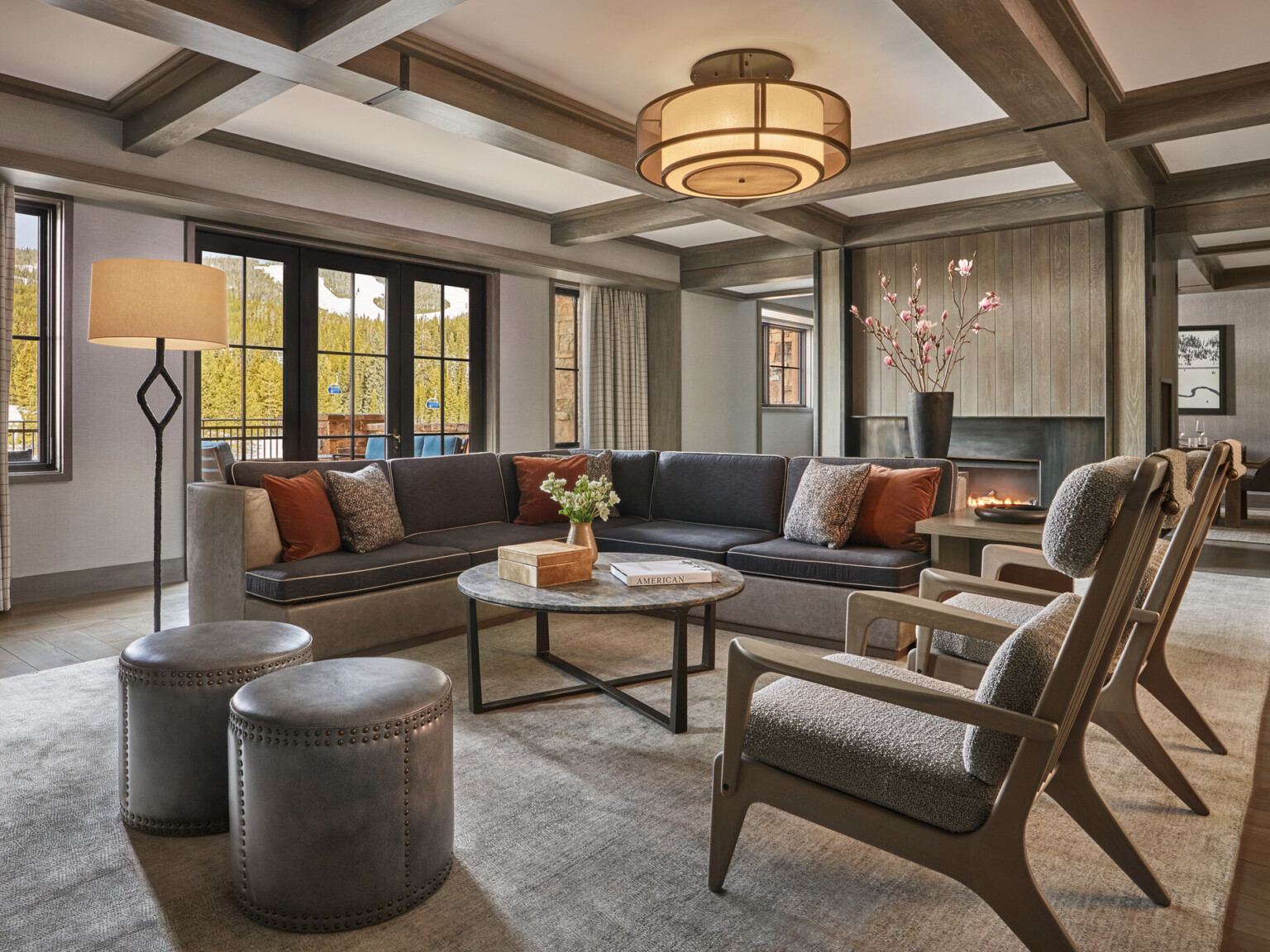 A modern living room with a large sectional sofa, coffee table, armchairs, and a fireplace, featuring neutral tones and natural lighting