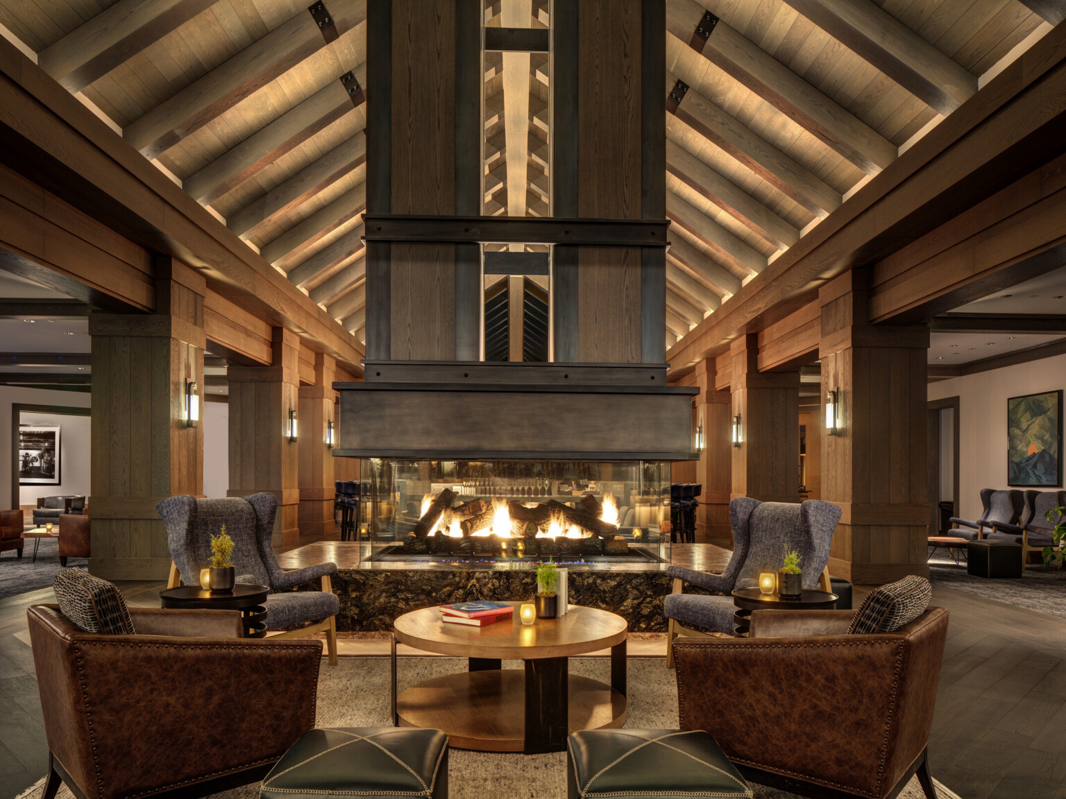 Cozy hotel lounge with a large double-sided fireplace, wooden ceiling beams and columns, and elegant seating arrangements throughout