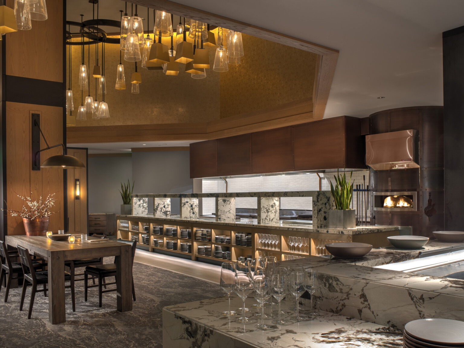 Modern hotel restaurant interior with a dining table, marble countertop, and open kitchen.