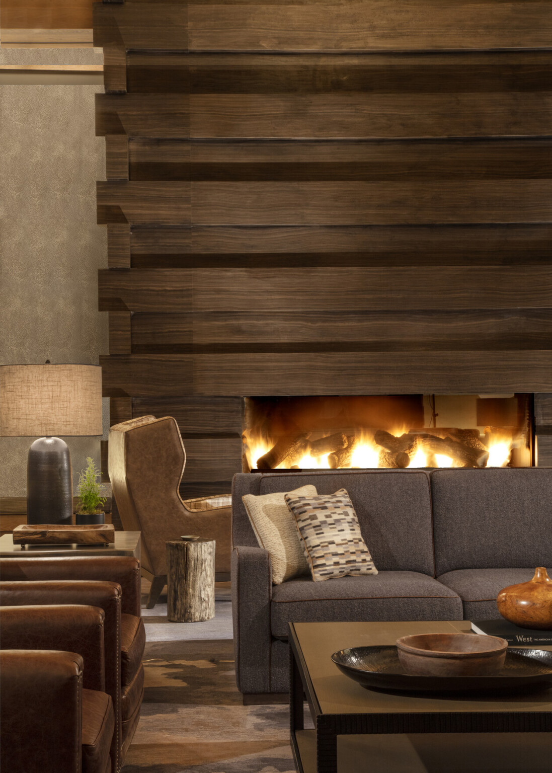 Cozy hotel lounge with gray sofa in front of a lit fireplace, coffee table, armchairs