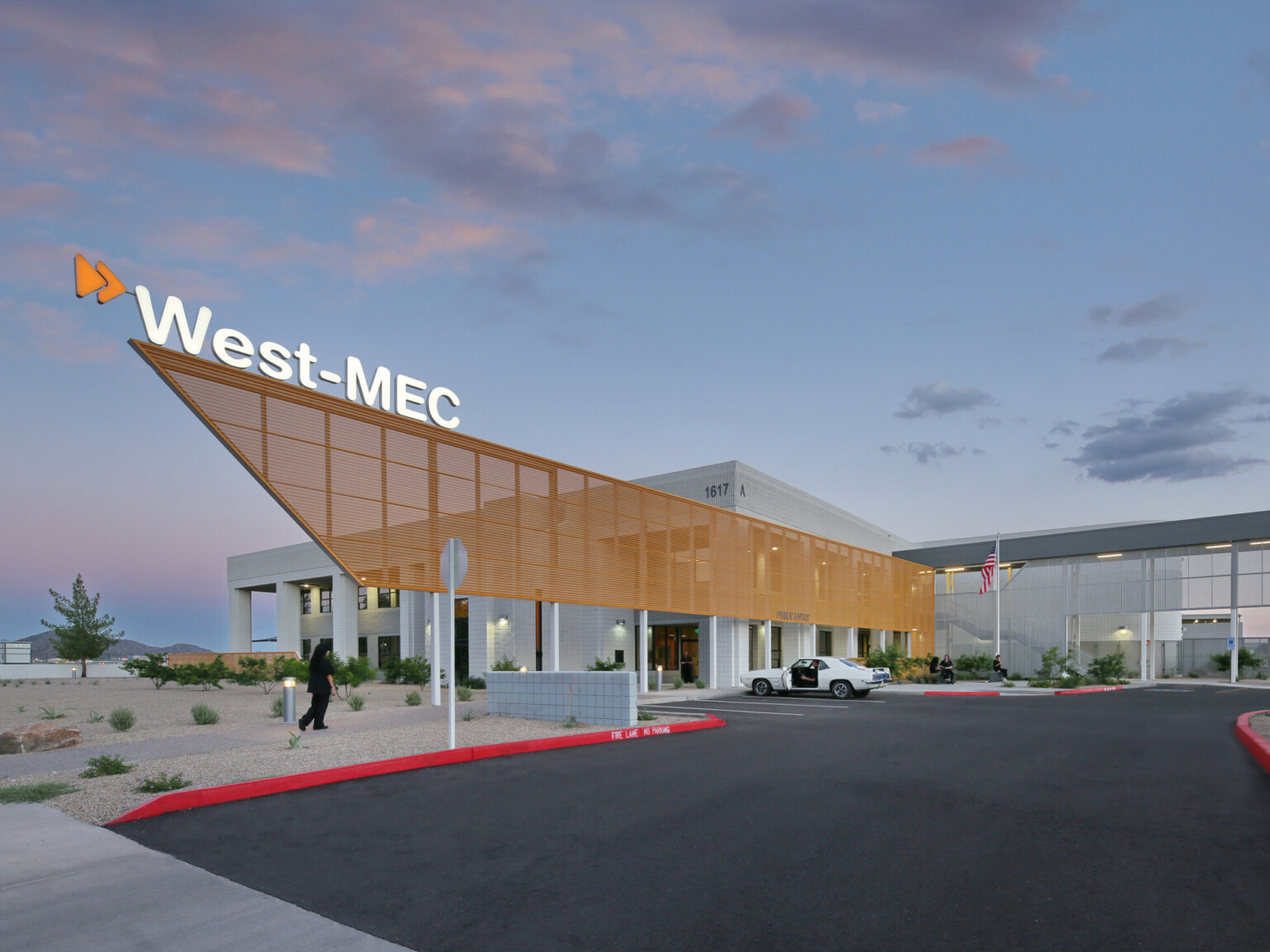 West-MEC Northeast Campus entrance with illuminated sign on top of orange perforated sunscreen extending past entrance