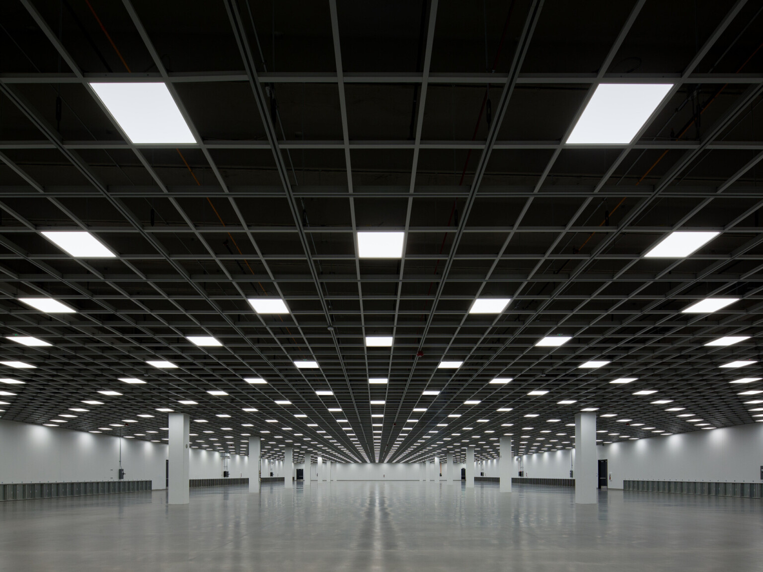 Large empty room with grid-patterned ceiling and fluorescent lights.