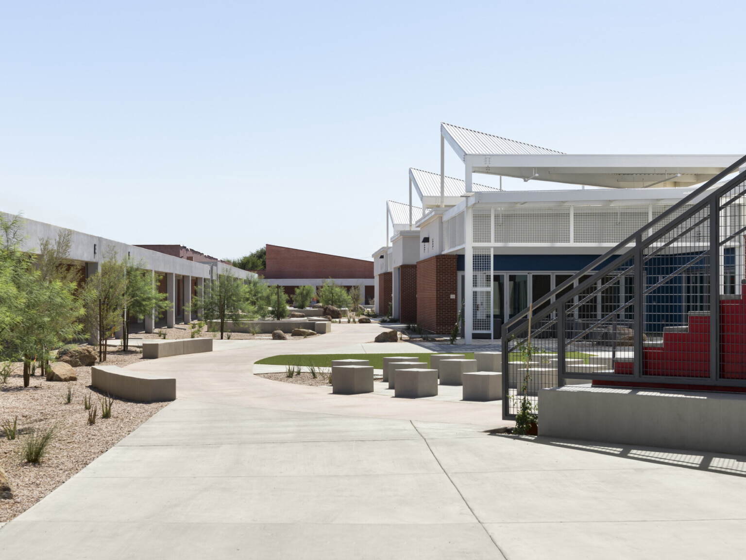 exterior of the quad, red stairs, white building with angular steel roof, concrete pathways