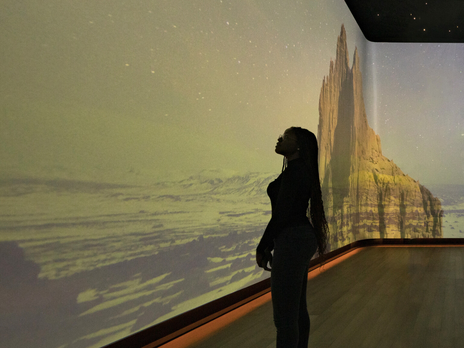 An immersive art exhibit at the Heard Museum with screens on all visible walls of the room showing the canyon desert hills colorized with soft shades of blue green and golden brown