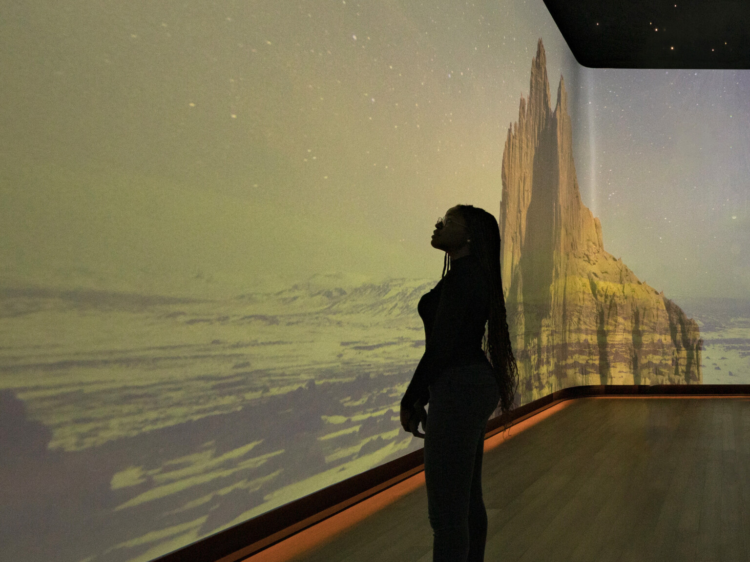 An immersive art exhibit at the Heard Museum with screens on all visible walls of the room showing the canyon desert hills colorized with soft shades of blue green and golden brown