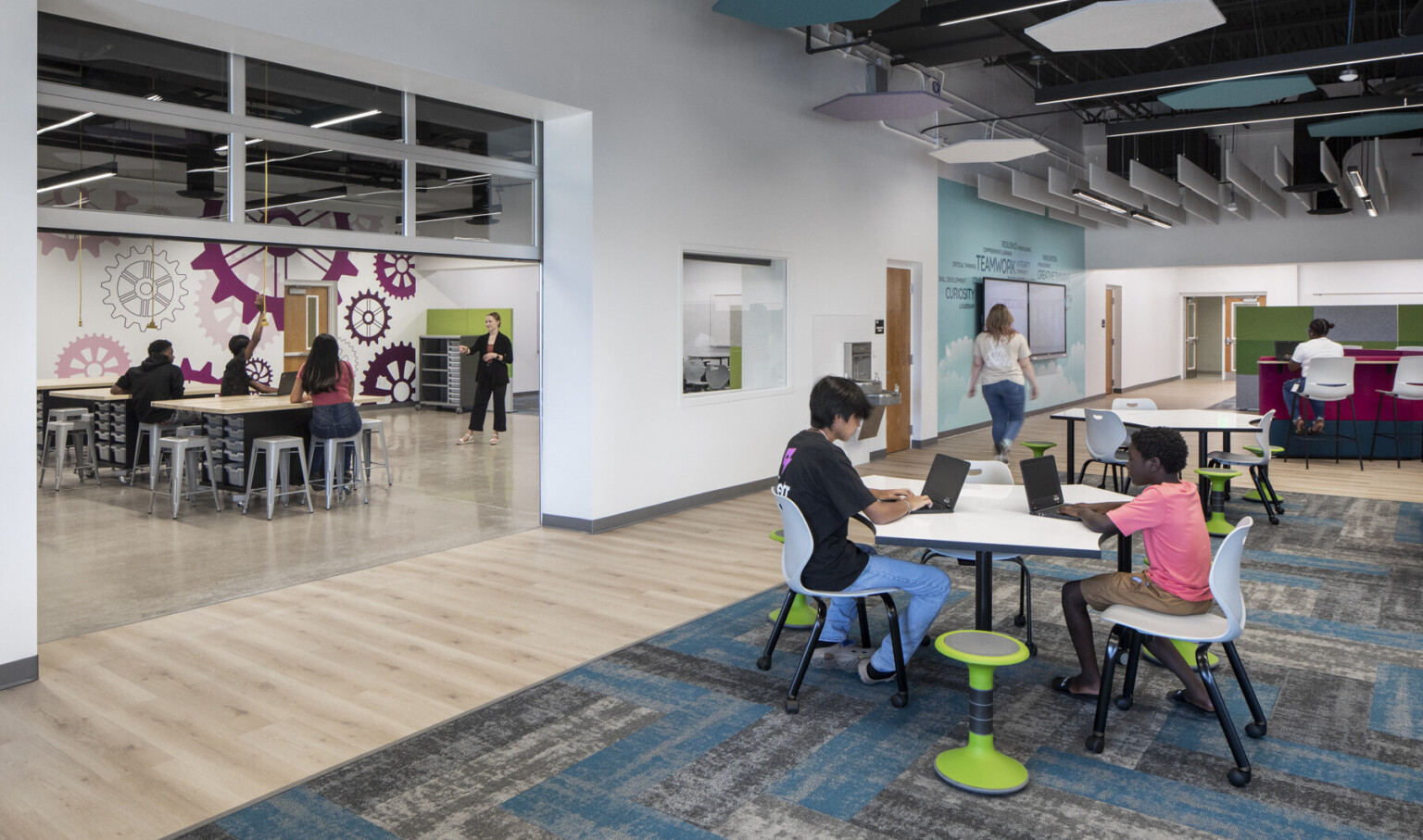 Open learning space inside a school with white walls, modern carpet and furniture, and an roll up door that is open looking inside a classroom