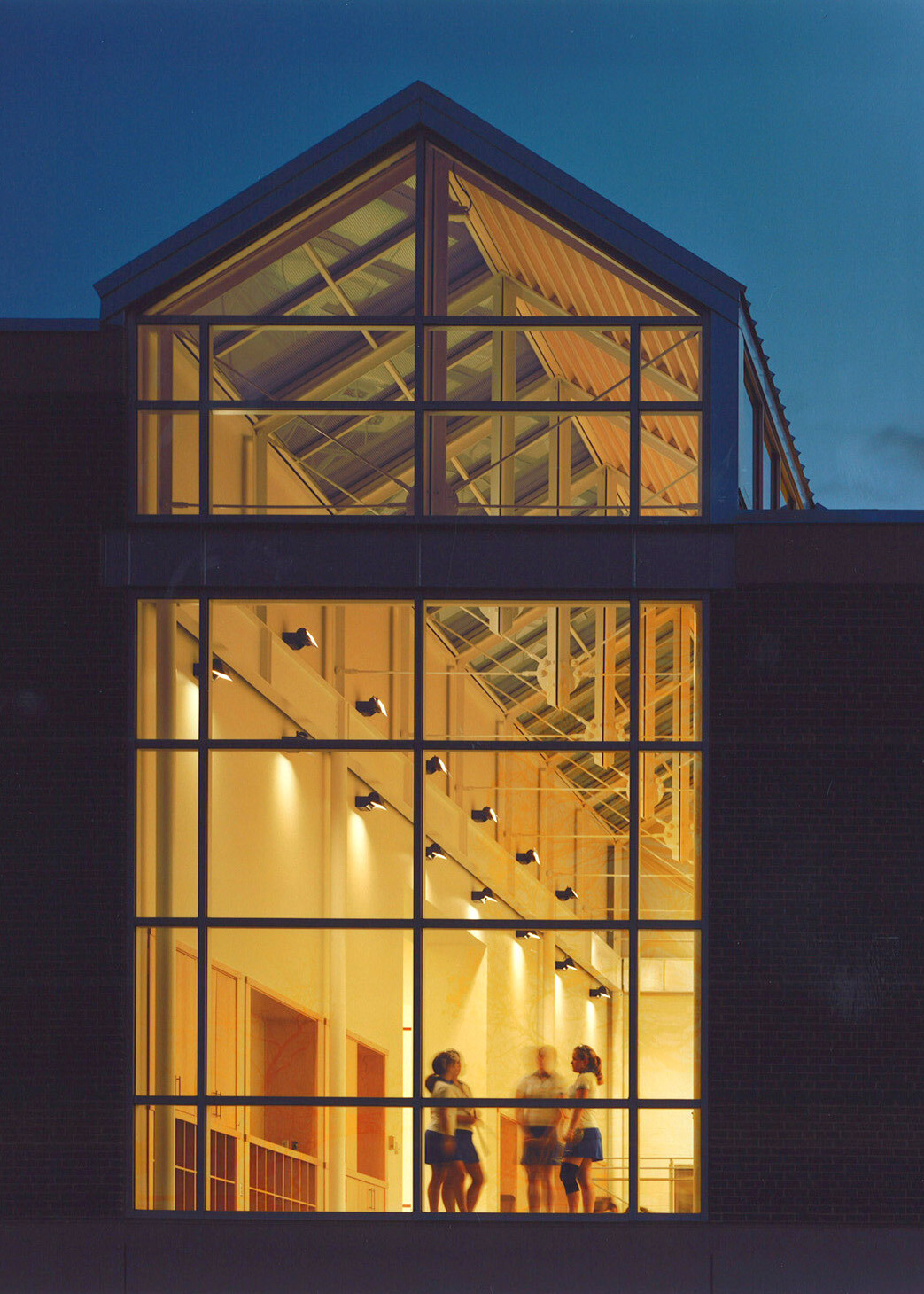 Nighttime view of a multistory building showing windows filled with light with students interacting inside