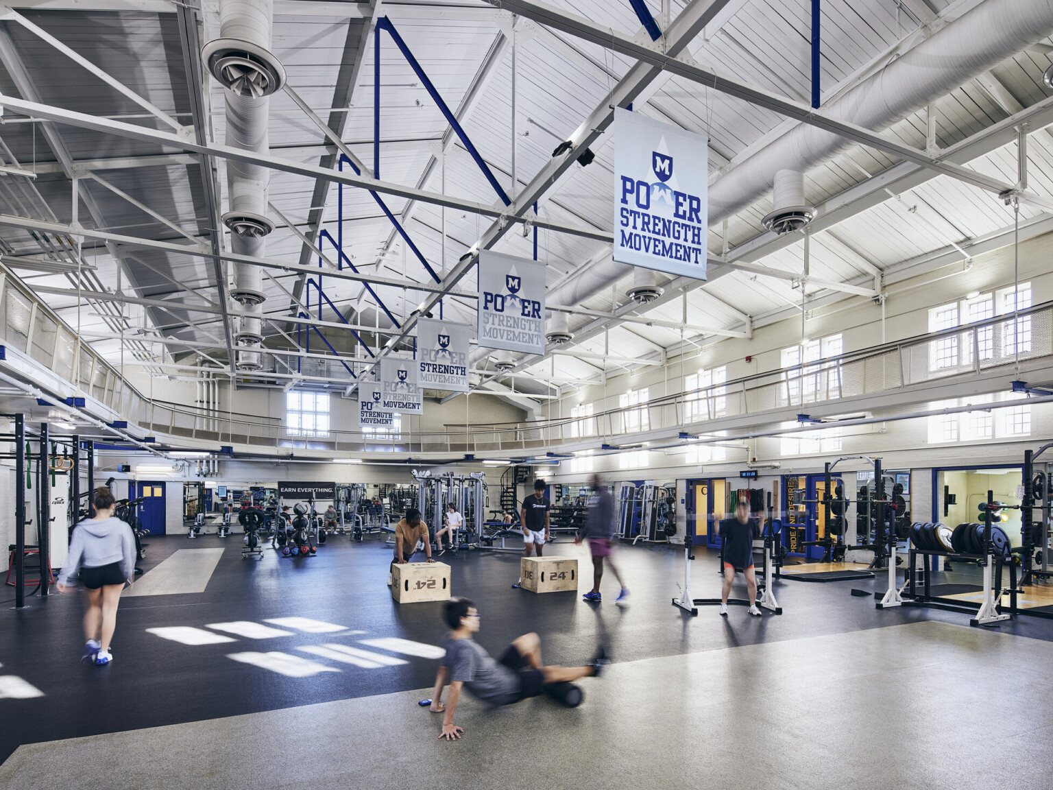 Indoor weight room filled with gym equipment on dark floors and people working out