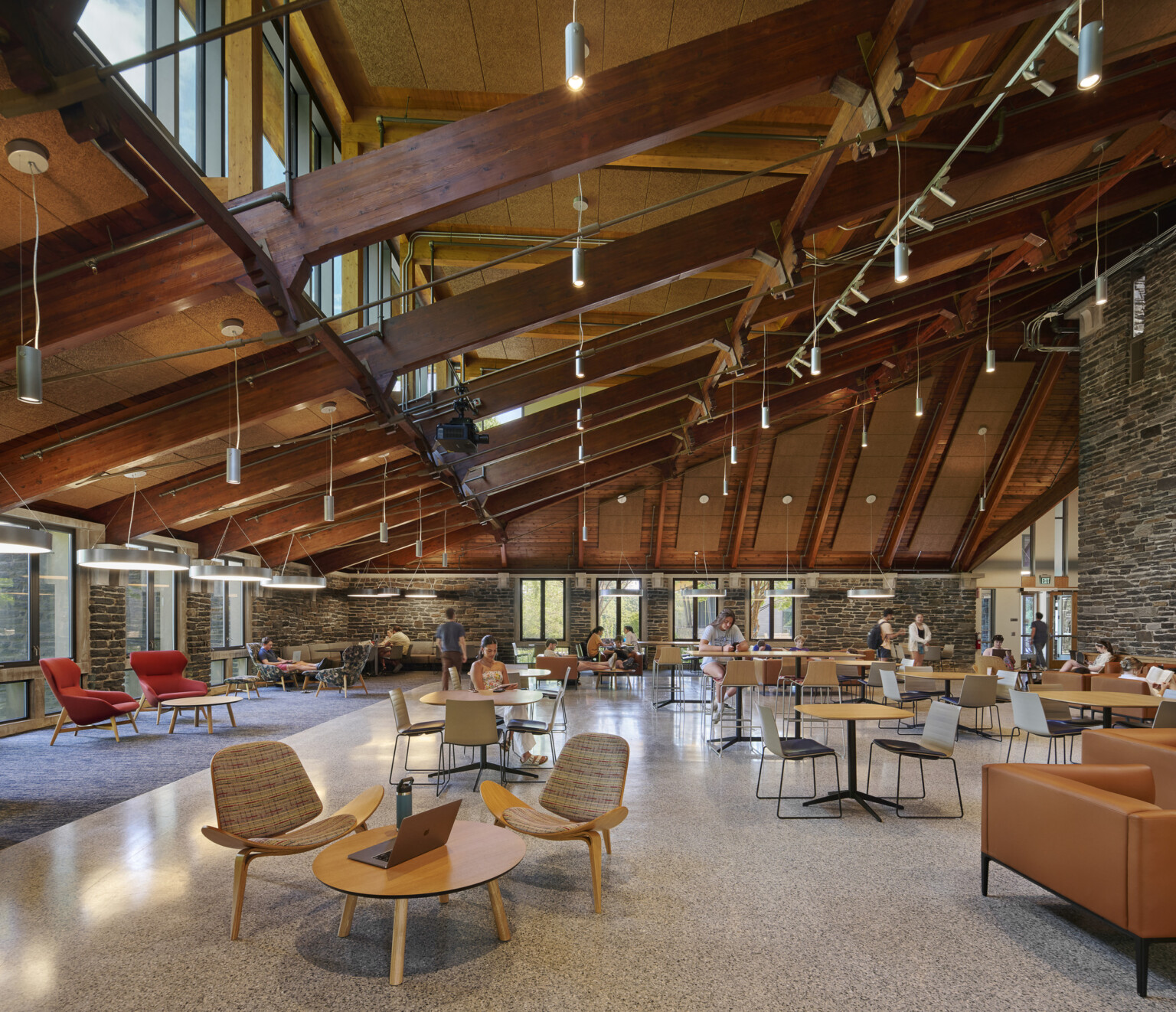 College common area filled with seating, exposed beams in the ceiling, and surrounded by exposed rock walls