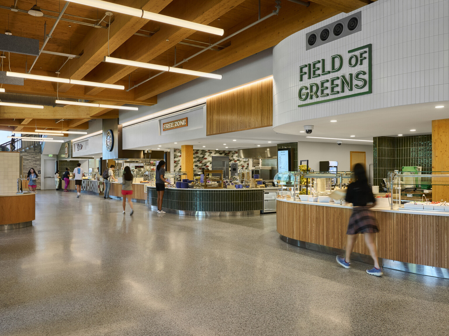 College dining hall with tall ceilings, exposed mass timber wood ceiling, green and white tile accents, raw concrete floors