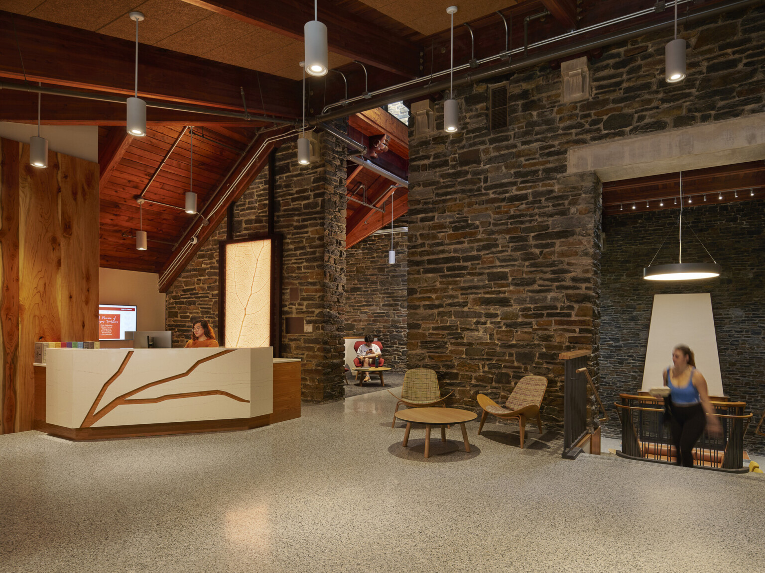 Interior common space with reception desk, exposed mass timber accent walls and ceiling, rock stone walls, pendant lights