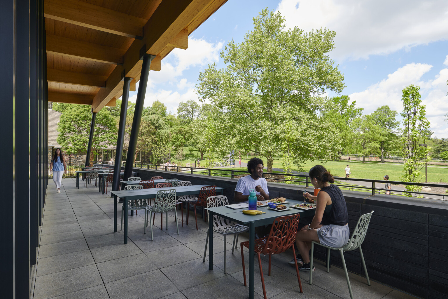 Outdoor dining area filled with tables and chairs overlooking lush trees and grass