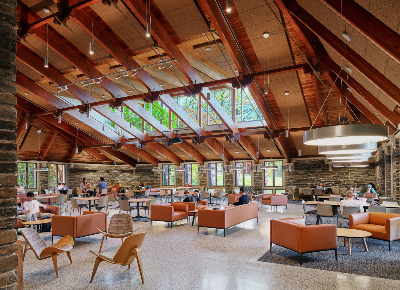 College common area filled with seating, exposed beams in the ceiling, and surrounded by exposed rock walls