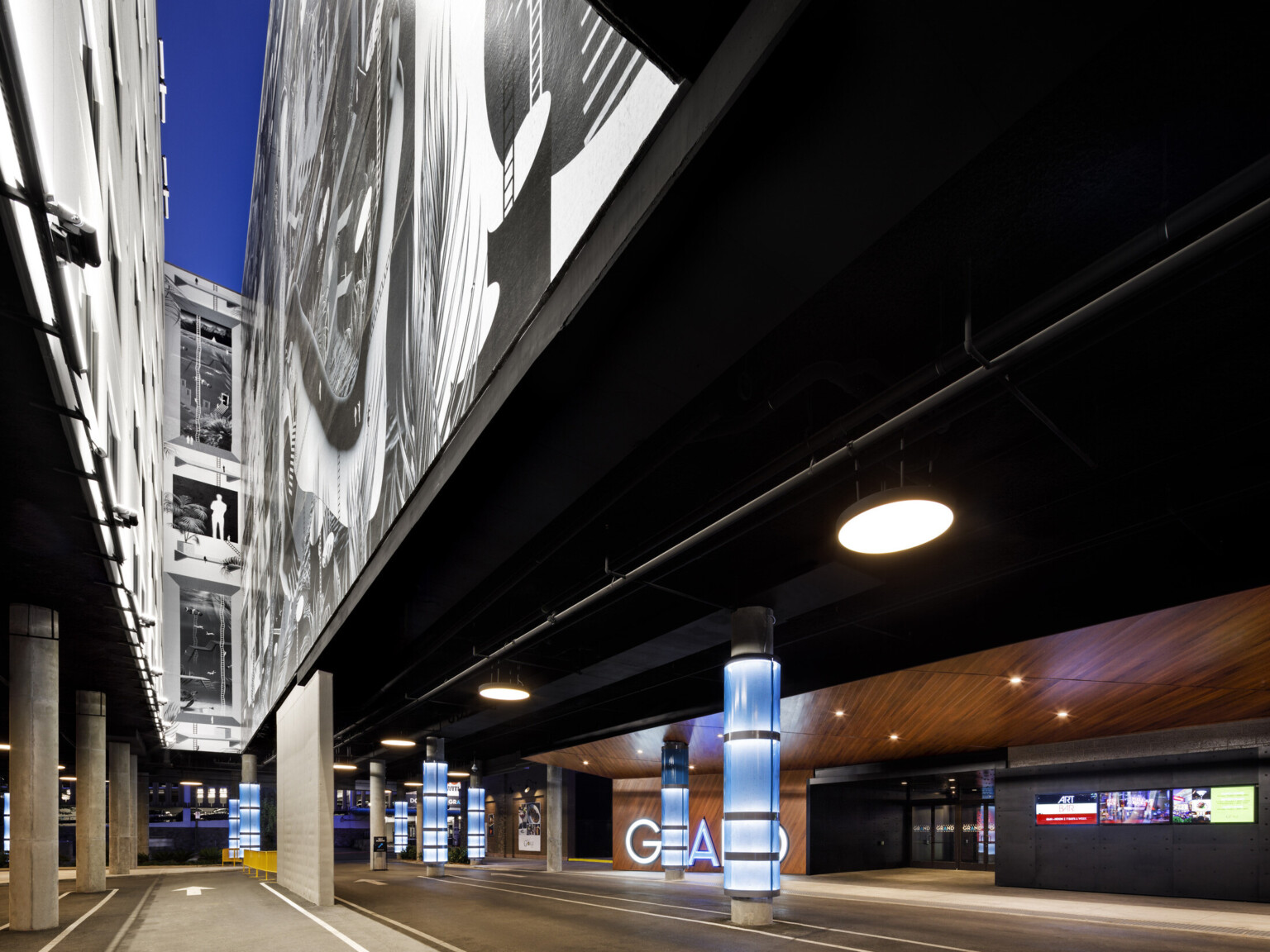 Standing on the ground looking up at a space between two buildings. Columns illuminated by blue light, wooden accents on wall and ceiling