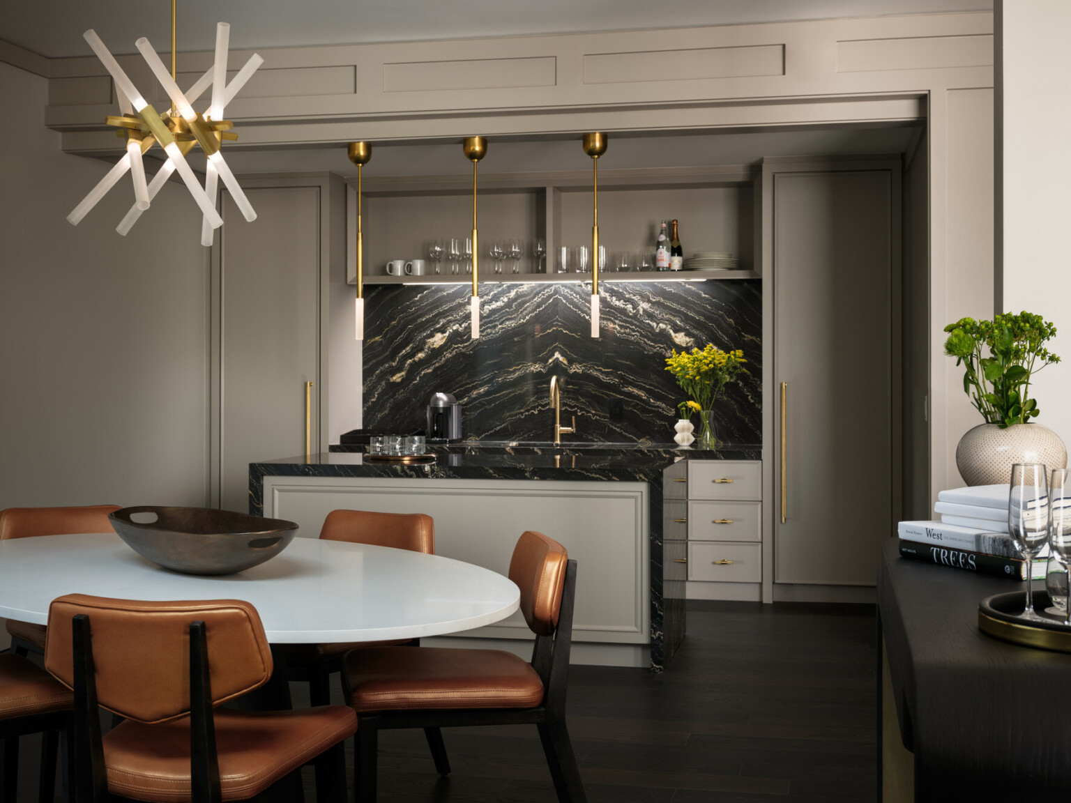 Seating area with white table and copper colored chairs in front of a island with black marble backsplash and counter with gold fixtures