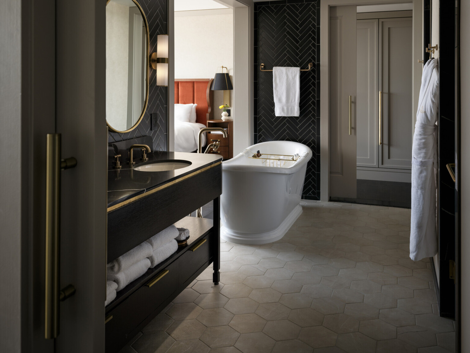 Bathroom with large white freestanding tub, black herringbone floor to ceiling tile, gold fixtures and accents throughout