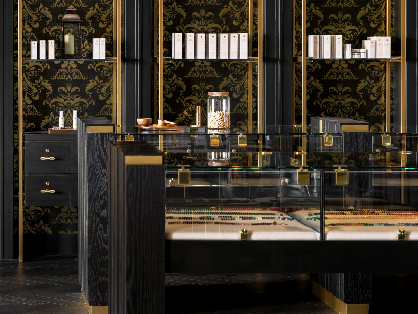 Black and gold shelves filled with objects, glass cases with black and gold accents, black flooring, black wallpaper with gold accents