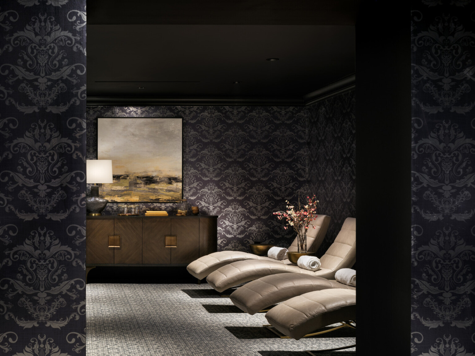 Dimly lit luxurious spa area with black and silver wallpaper, gold lounge chairs, with bronze furnishings