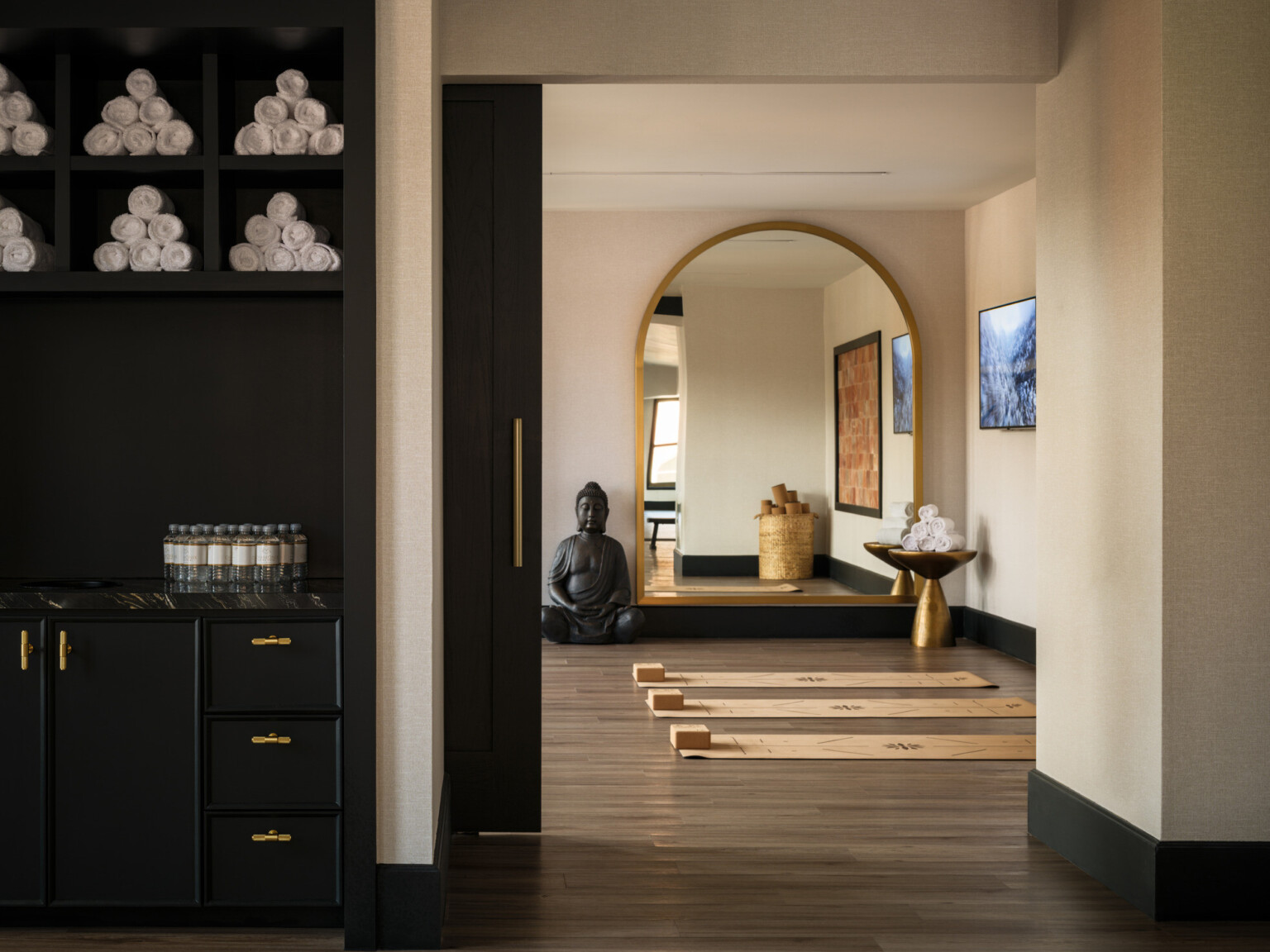 Modern yoga room, with dark shelves filled with towels, yoga mats with blocks on the floor, large arched mirror on back wall