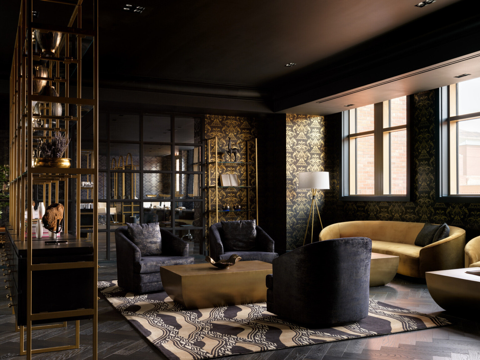 Dramatic seating area with black wallpaper filled with designs in gold, gold couches, black chairs, black and gold shelves