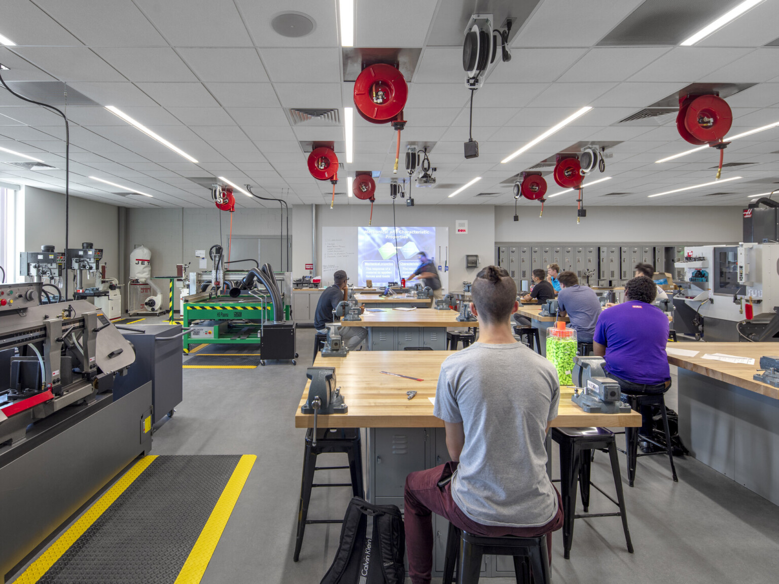 Classroom with equipment along left wall. Tables and stools in rows, right, with extension cords dispensed from above