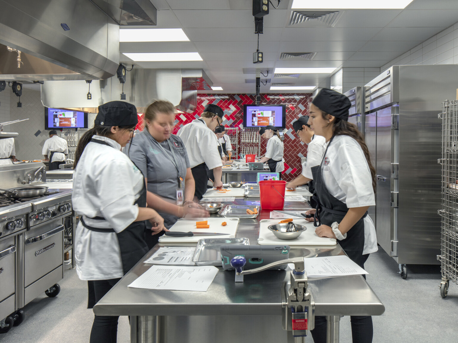 Culinary kitchen classroom with stainless steel island and red tile back wall. Stoves on left wall, refrigerators to right, cherry creek innovation campus