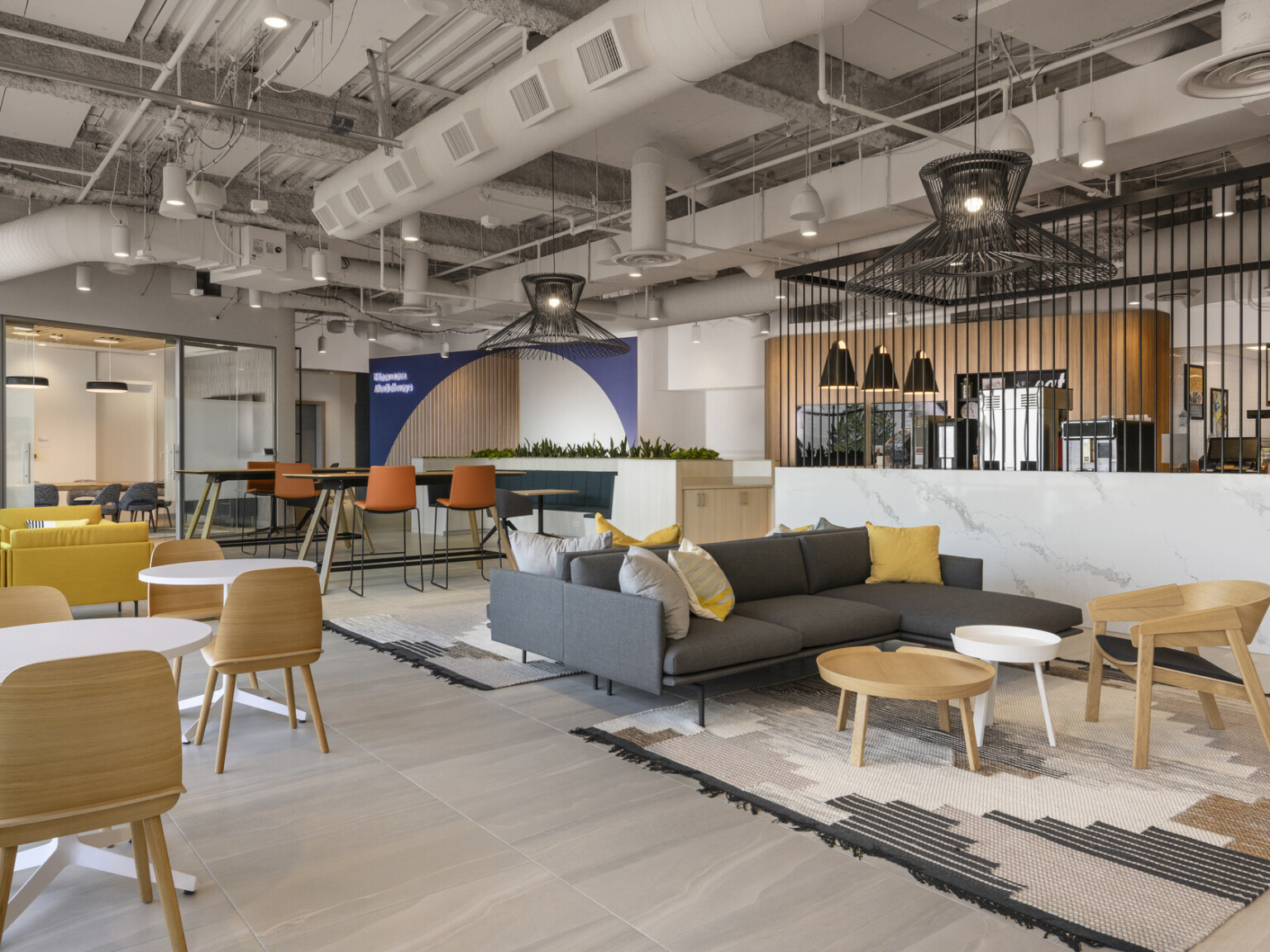 Lounge space with multiple seating areas with wire pendant lights. marble half wall, right, below metal partition. Exposed ductwork above on white ceiling