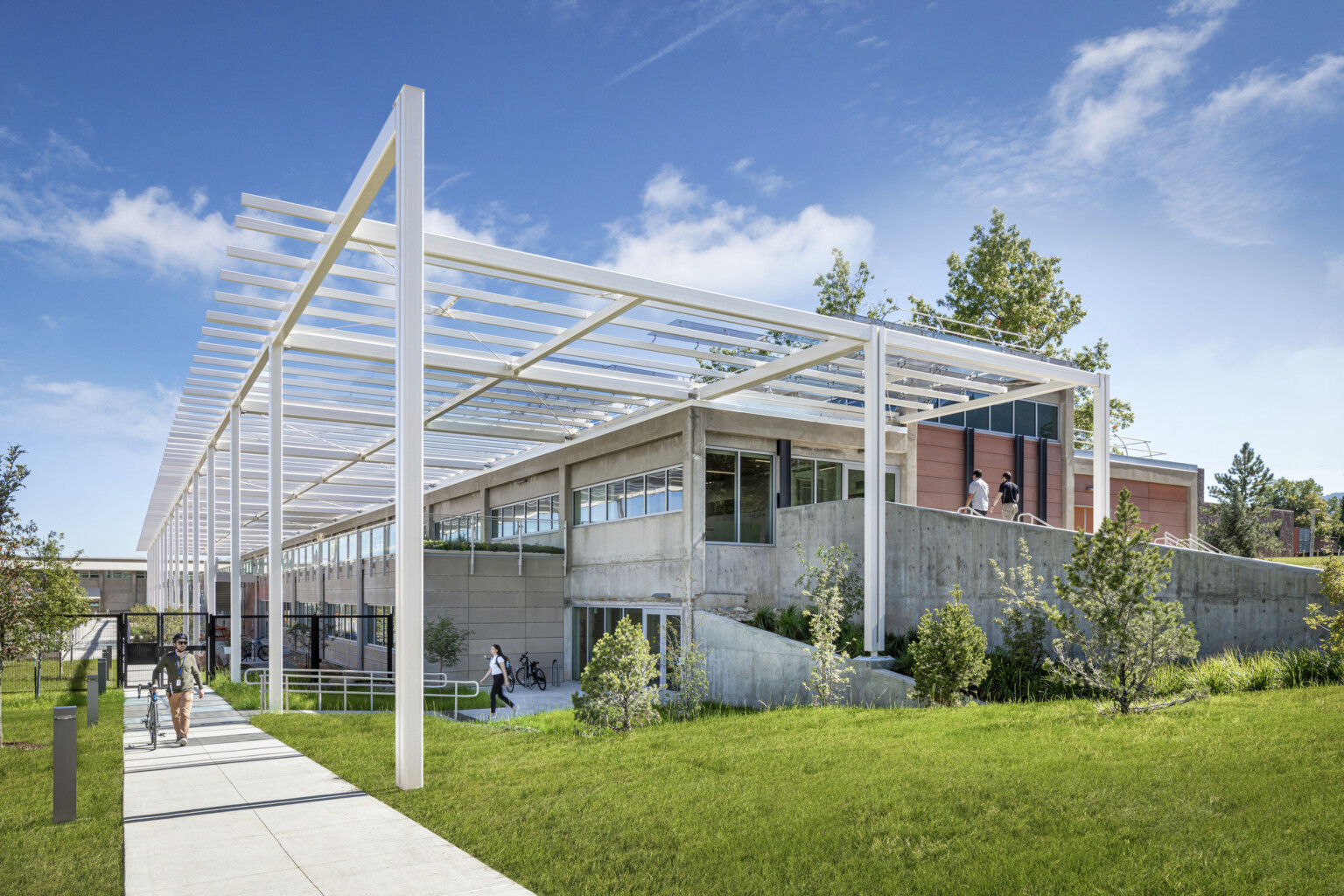 Modern multistory building built into a hill with white metal decorative columns and lush landscaping