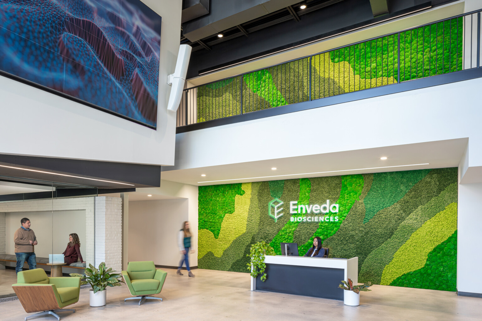 living green wall with company Envada signage, front desk to workplace, double height atrium with black railing along upper level