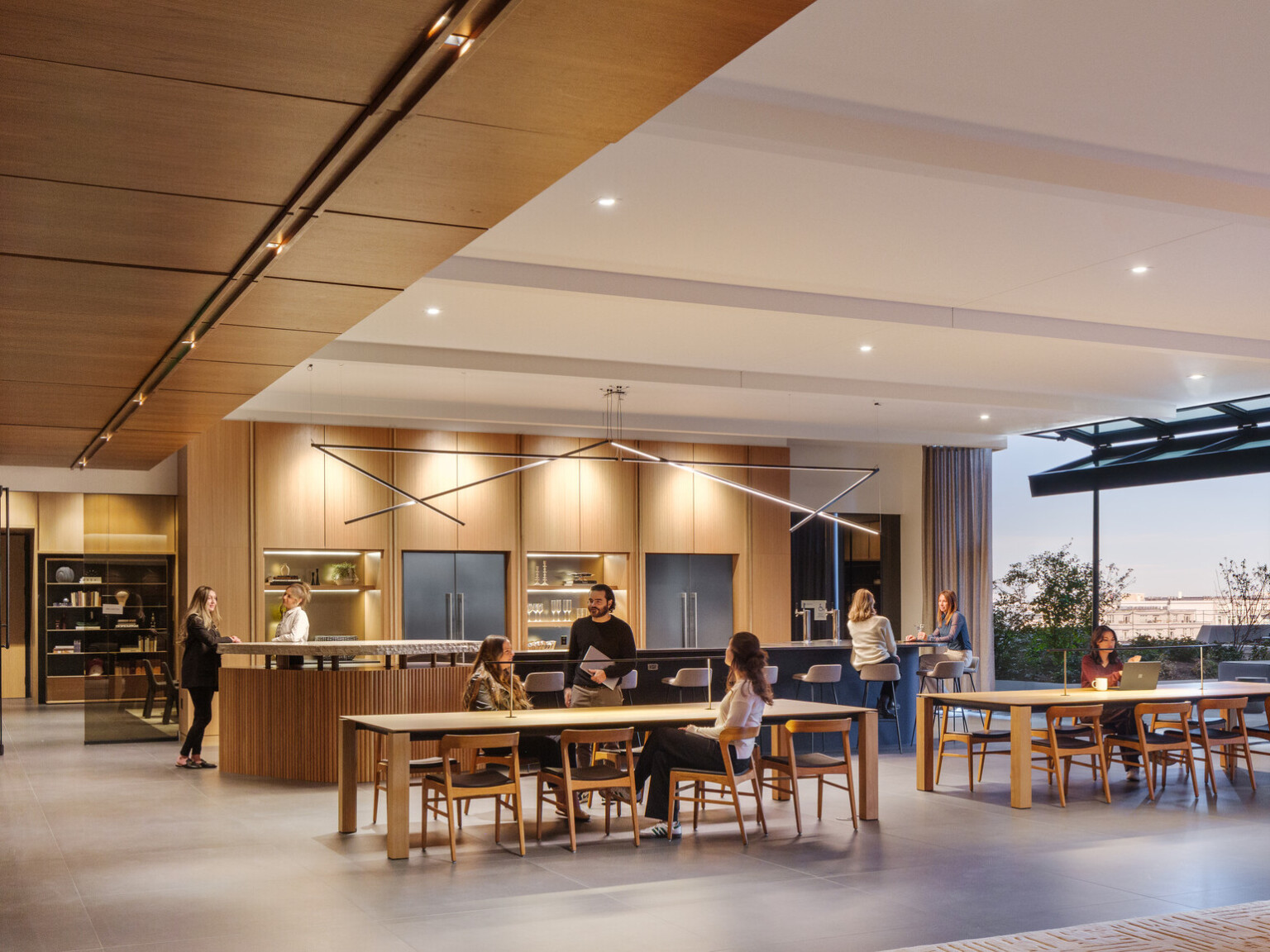 A modern office space with wooden decor, people interacting at tables, and large windows offering outdoor views.