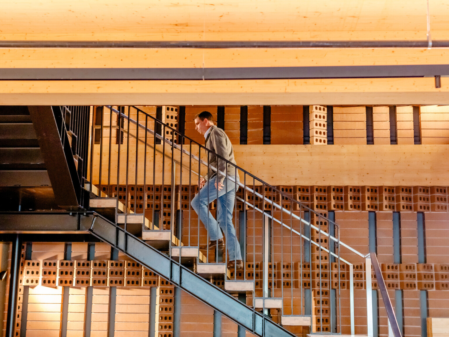 A person walking up a metal and wooden staircase in a building with exposed brick walls.